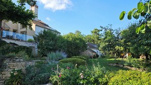 Um jardim com muros de pedra, diversas plantas e um edifício com telhado de azulejos.