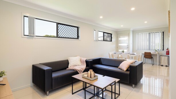 A modern living room with a black leather sofa, a coffee table, and a dining area with a table and chairs. - Smart Suites Self Check-in Apartments - 20 Darnley (Rocklea)