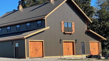 A two-story building with a gabled roof, large wooden doors, and a small window with shutters.