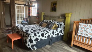 A room with a bed, a wooden bench, a crib, and a window.