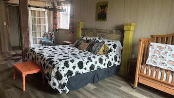 A room with a bed, a wooden bench, a crib, and a window.