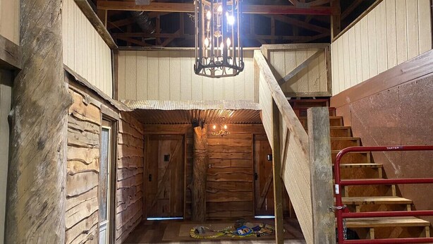 A rustic interior with wooden walls, a wooden staircase, and a chandelier.