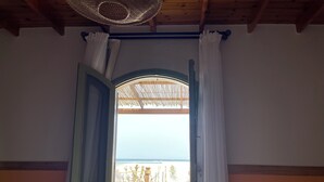 An open door leading to a patio with a view of the sea, wooden furniture, and a thatched roof structure.