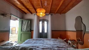 A bedroom with a bed, a wooden ceiling, a green door, and a window with curtains.
