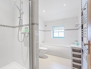Ein modernes Badezimmer mit Duschkabine aus Glas, einer weißen Toilette, einer Badewanne und einem kleinen Fenster.
