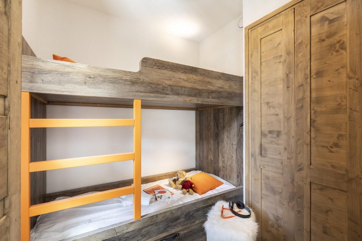 Ein Etagenbett mit Holzlade, einer weißen Matratze und einem kleinen Regal mit Büchern und Spielzeug.