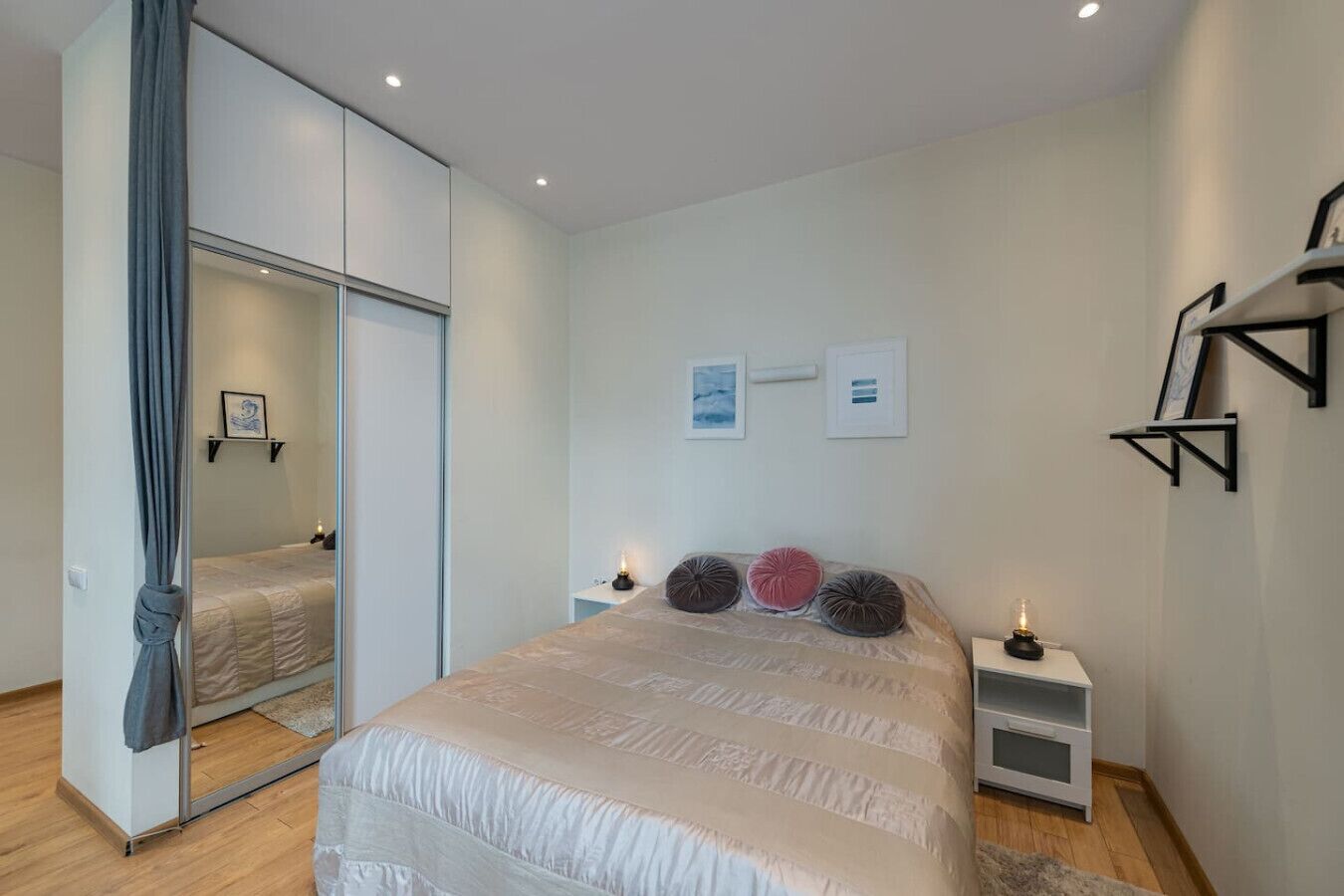 A bedroom with a bed, bedside tables, a mirror, and wall-mounted shelves.