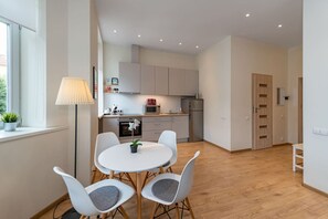 A modern kitchen with white cabinets, a dining area with a round table and chairs, and a wooden floor.