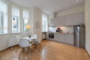 A modern kitchen with a dining area, large windows, and a refrigerator.