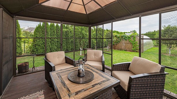 A covered patio with wicker furniture and a central table, large windows offering a view of a garden and trees. - Calm and private ap by Polo Apartments (Kaunas)