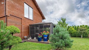 A wooden house with a glass conservatory, a well-maintained lawn, and various potted plants. - Calm and private ap by Polo Apartments (Kaunas)