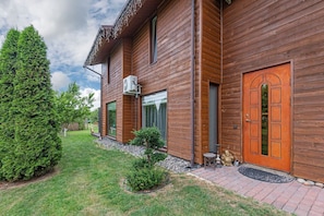 Een houten huis met een grote boom, een kleine tuin en een verharde oprit.