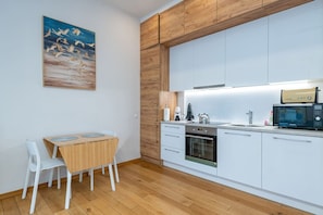 A modern kitchen with white cabinets, a wooden dining table, and a painting of birds on the wall.