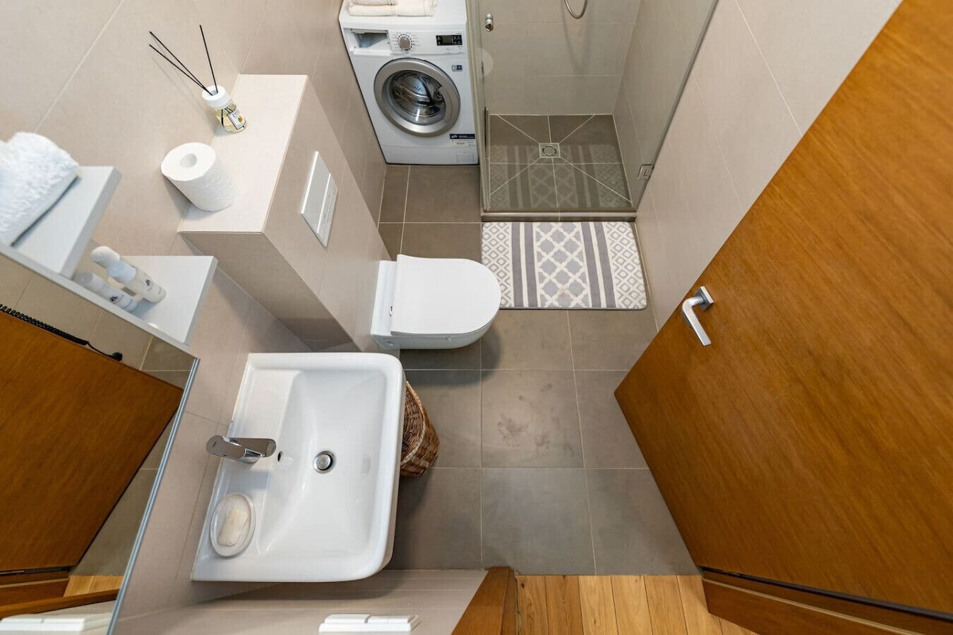 Un baño pequeño pero funcional con lavamanos, inodoro, lavadora y zona de ducha.