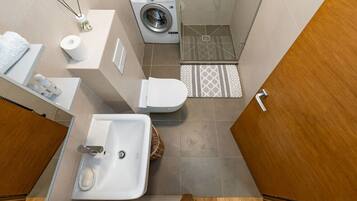 Un baño pequeño pero funcional con lavamanos, inodoro, lavadora y zona de ducha.