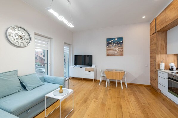 A modern living room with a sofa, TV, dining table, and kitchen area.