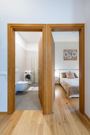A room with a bed, a nightstand, a wall-mounted artwork, and a wooden floor.