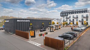 Un restaurant McDonald's doté d’une façade noire moderne, un parking avec des voitures et, au fond, un bâtiment avec des balcons.