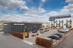 A McDonald's restaurant with a modern black facade, a parking lot with cars, and a building with balconies in the background.