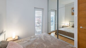 Une chambre à coucher comprenant un lit, une table de chevet, une commode, un miroir et une porte-fenêtre coulissante donnant sur un balcon.