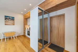 A room with a wooden floor, a dining table with chairs, a kitchen area, and a sliding door.