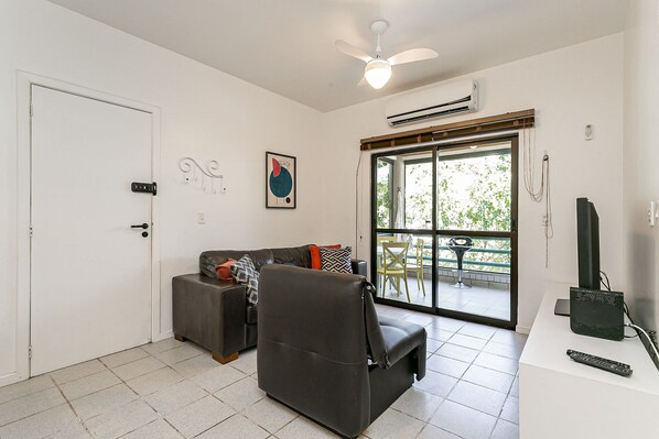 A living room with a sofa, a chair, a TV, and a balcony with a table and chairs.