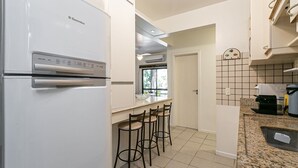 A kitchen with a white refrigerator, a countertop, and three bar stools. - 200m from Beach | Bbq Grill | Swimming Pool #IA29 (Florianópolis)