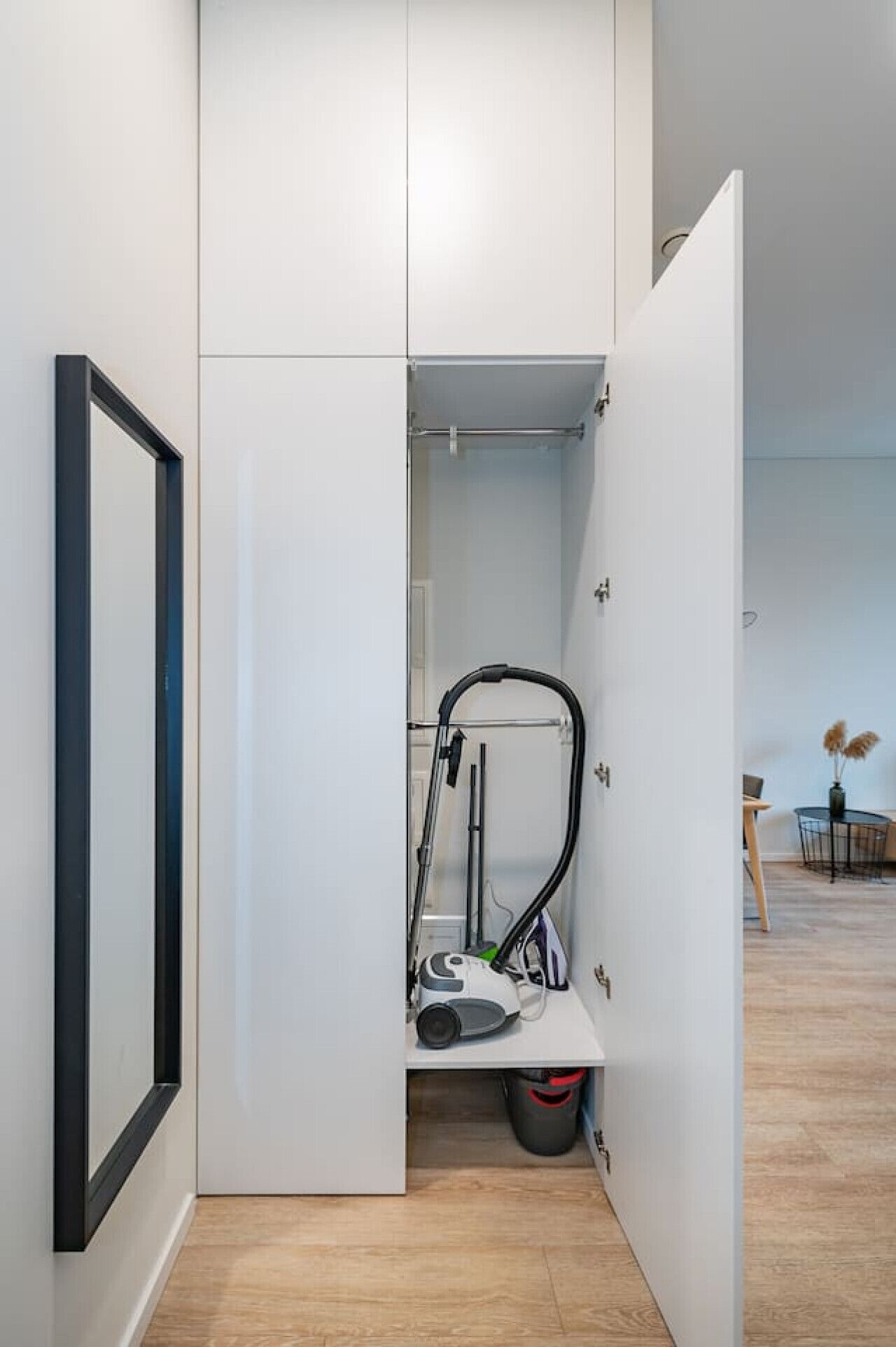 Een compacte kamer met een inbouwkast, een klein zithoekje met een tafeltje, en een stofzuiger.