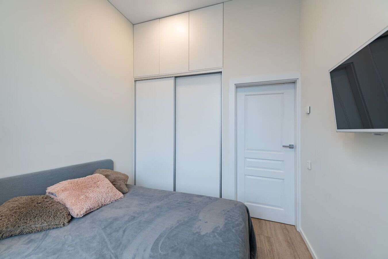 A bedroom with a bed, a wardrobe, and a TV mounted on the wall.