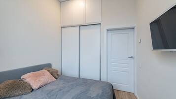 A bedroom with a bed, a wardrobe, and a TV mounted on the wall.