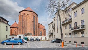 Uma igreja com fachada de tijolos e telhado vermelho, rodeada por edifícios altos com varandas.