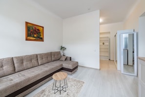 Un salon moderne avec un canapé d’angle, un petit tabouret en bois, une plante en pot et un tableau accroché au mur.