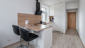 A modern kitchen with a wooden countertop, two black bar stools, a kettle, a microwave, and a black range hood.