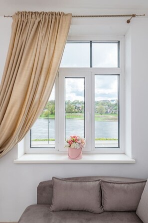Um quarto com janela, sofá e um vaso com flores.