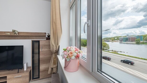 A modern living room with a TV, wooden cabinet, and a window with a view of a river and buildings.