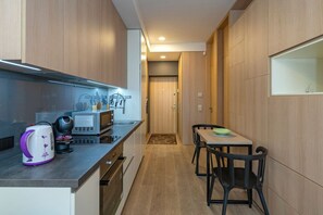 A compact kitchen with a microwave, kettle, and coffee maker on the counter, a dining area with a table and chairs, and wooden cabinetry.
