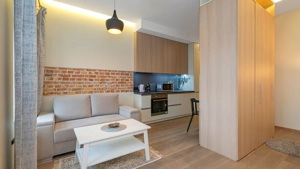 A modern living room with a sofa, a coffee table, and a kitchen area with wooden cabinets and appliances.