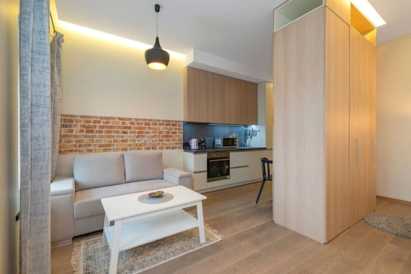 A modern living room with a sofa, a coffee table, and a kitchen area with wooden cabinets and appliances.