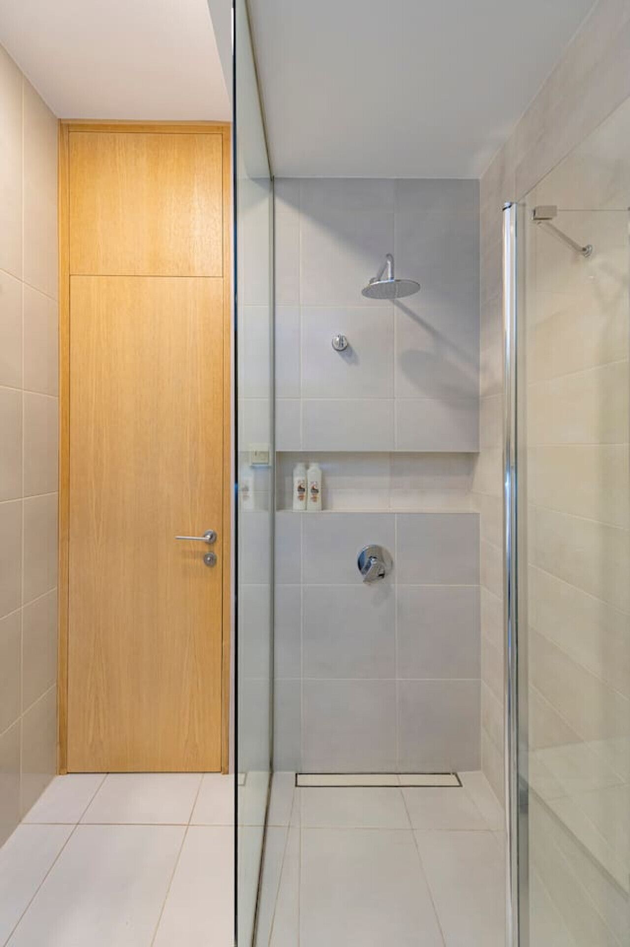 Un baño moderno con puerta de madera, cabina de ducha de vidrio y paredes con azulejos.