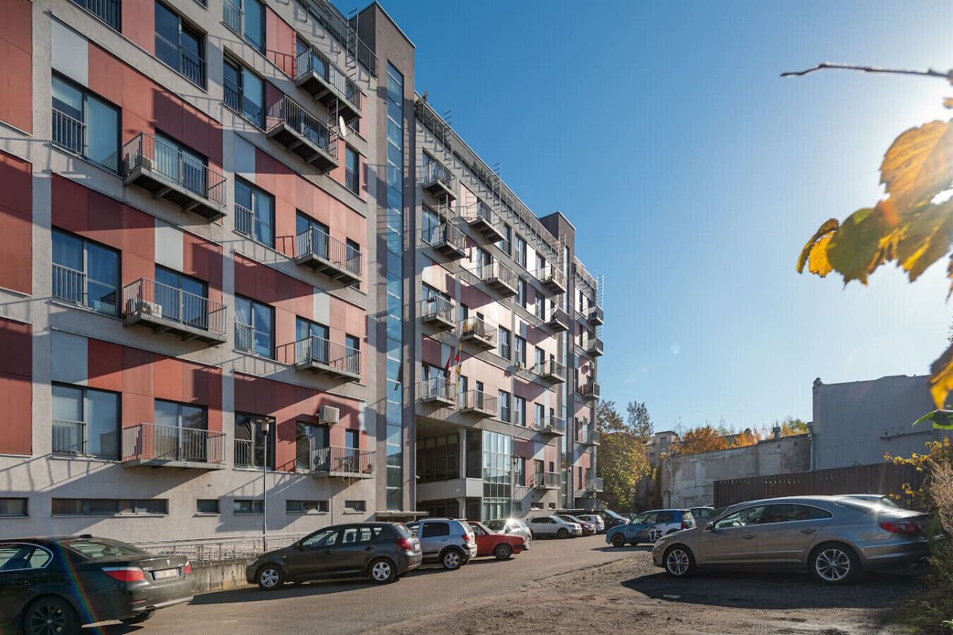 Ein mehrstöckiges Wohngebäude mit Balkonen, parkgeparkten Autos und blauem Himmel.
