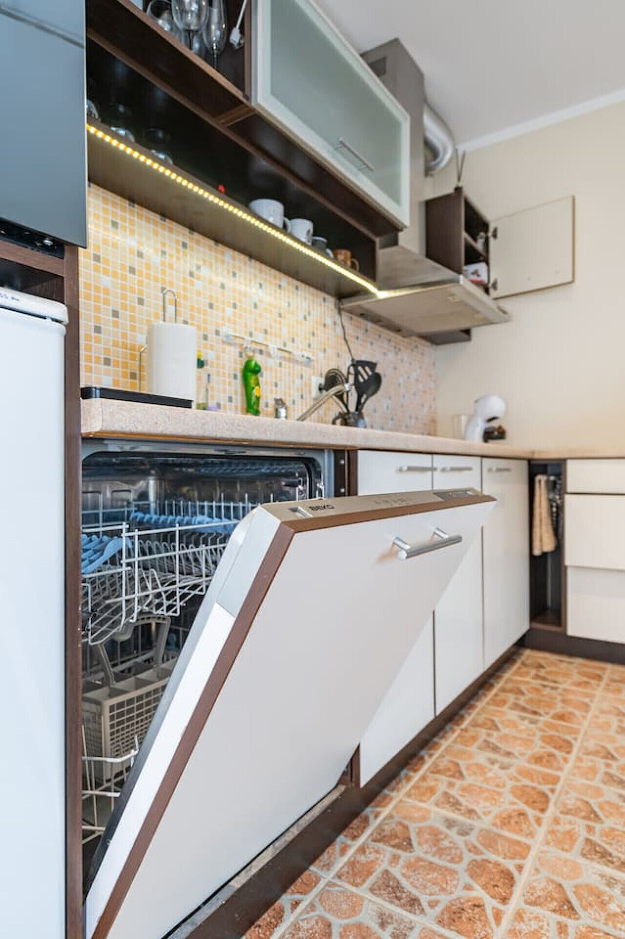 A kitchen with a dishwasher, tiled backsplash, and a stone-patterned floor.