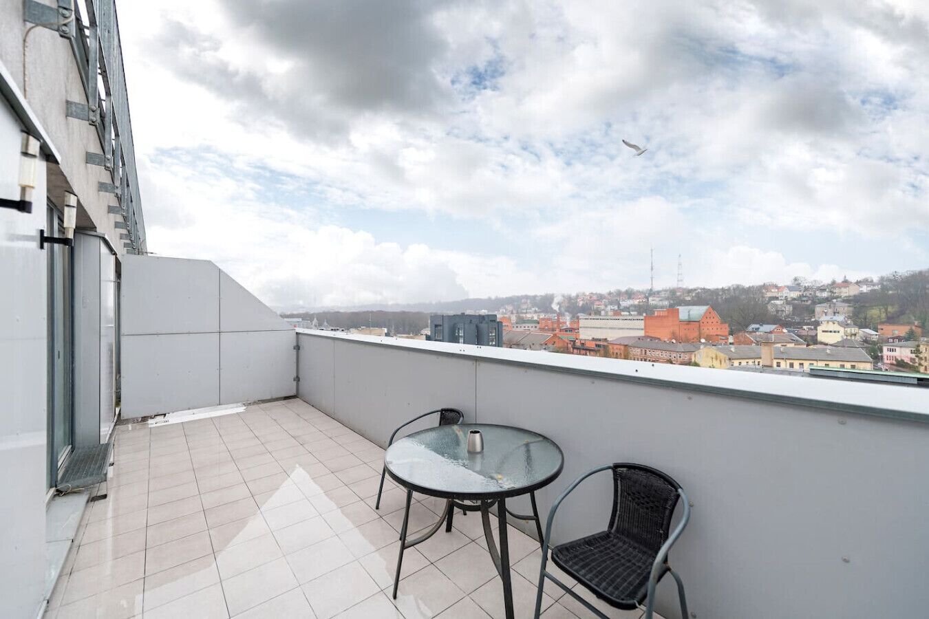 Ein Balkon mit Fliesenboden, einem Glastisch und zwei Stühlen.