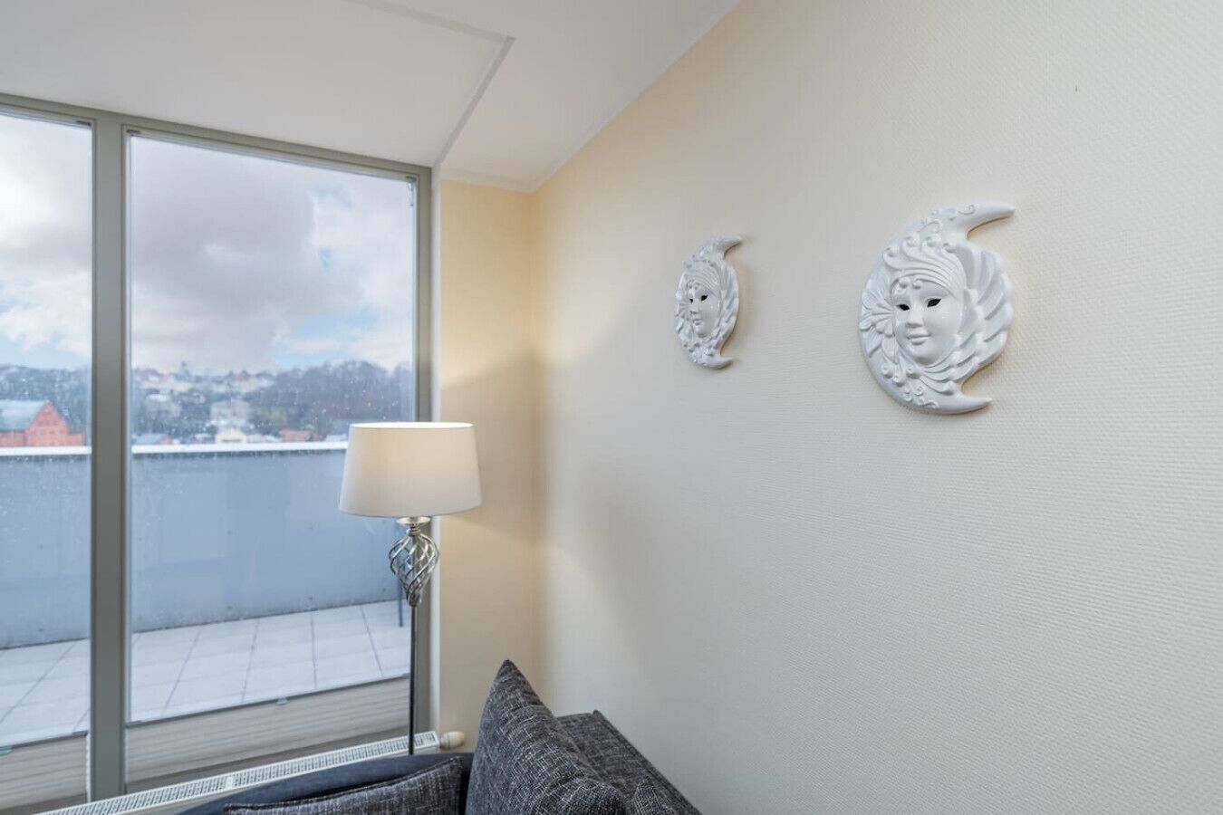 A room with a large window, a lamp, and two wall decorations.
