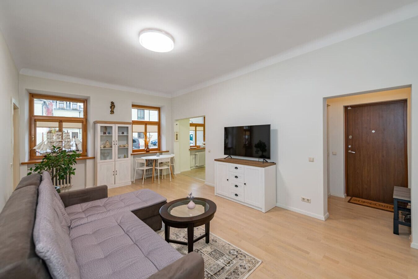 A spacious living room with a sofa, a television, a cabinet, and a dining area with a table and chairs.