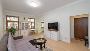 A spacious living room with a sofa, a television, a cabinet, and a dining area with a table and chairs.