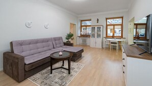 Ett vardagsrum med en soffa, ett soffbord, en matplats med bord och stolar samt ett köksområde med skåp och ett kylskåp.