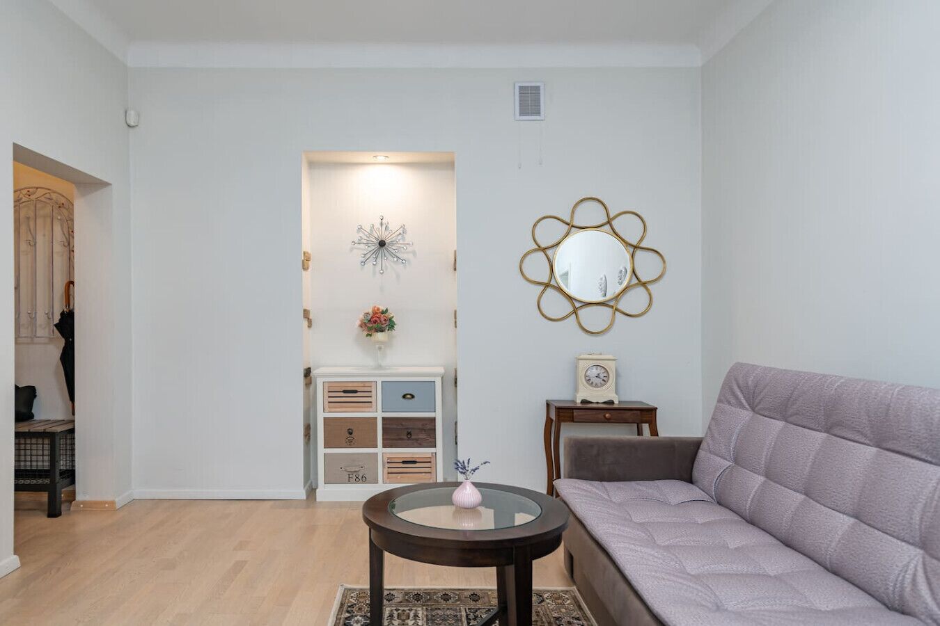 Een woonkamer met een bank, een rond bijzettafeltje, een decoratieve spiegel en een nachtkastje met een klok.