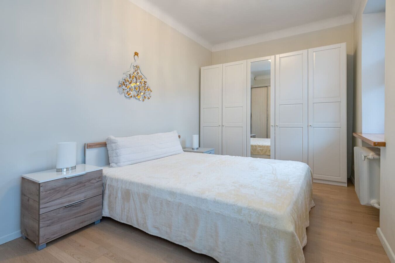 A bedroom with a bed, bedside tables, a dresser, a wardrobe, and a decorative wall piece.