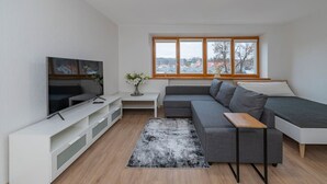 A modern living room with a TV, sofa, and large windows.