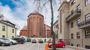 A church with a brick facade and a red roof, surrounded by modern buildings and parked cars.